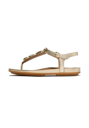 Gold flat sandal with ankle strap, buckle closure, and decorative gems on the T-strap, shown in side profile against white background.