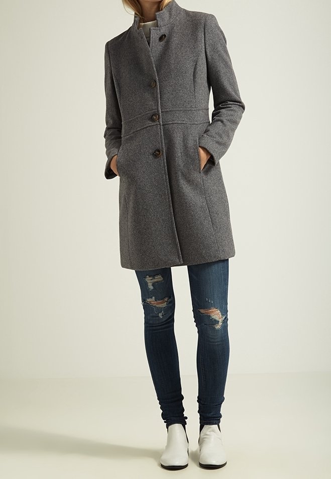 Gråullkappa med hög krage, fyra knappar och sidofickor, tillsammans med blå rivna jeans och vita ankelboots.