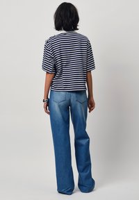 Gestreepte t-shirt in marineblauw en wit, korte mouwen, cropped lengte. Lichte blauwe wijdlopende jeans met een vervaagde wassing en achterzakken.