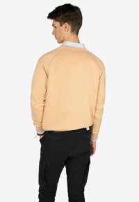 Beige sweatshirt met raglanmouwen, van katoenmateriaal, en een lichtblauwe kraagdetails. Zwarte cargo broek met meerdere zakken.