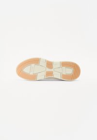 Shoe sole in beige with orange accents, featuring a textured rubber surface and a distinctive tread pattern for traction and grip.