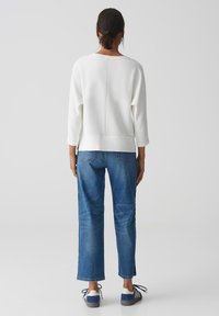 Witte geribbelde trui met 3/4 mouwen, gecombineerd met blauwe rechttoe rechtaan jeans en marineblauwe schoenen met witte accenten. Achteraanzicht.