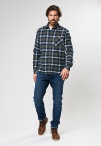 Flanellen shirt met een blauw, groen en wit ruitpatroon, met een button-down kraag, borstzak en lange mouwen, gecombineerd met donkere jeans en bruine laarzen.