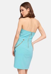 Un vestito aderente senza spalline in tessuto azzurro chiaro, con zip sul retro, arricciature laterali e dettagli in catena dorata sulle tasche.