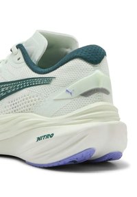 Scarpa da corsa bianca con upper in mesh e accenti turchesi. Presenta un tallone testurizzato, una suola viola e un logo "NITRO" ben visibile sul lato.