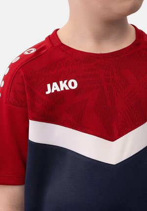 Chemise de sport rouge et marine avec un design en chevron blanc. Présente des motifs en relief sur le tissu rouge, avec le logo "JAKO" en blanc sur la poitrine.