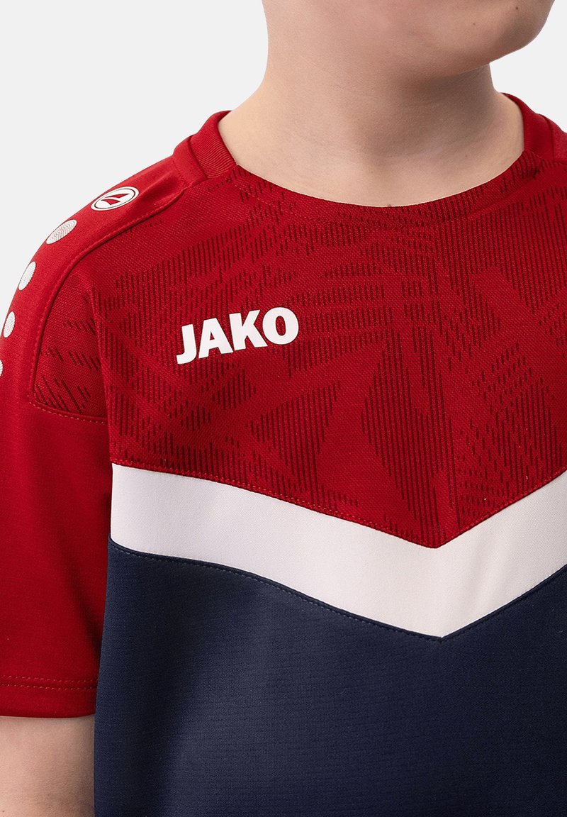 Chemise de sport rouge et marine avec un design en chevron blanc. Présente des motifs en relief sur le tissu rouge, avec le logo "JAKO" en blanc sur la poitrine.