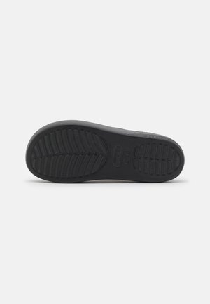 Semelle de chaussure en caoutchouc noir avec des motifs de grip texturés et un logo de marque au centre, présentée à plat sur un fond blanc uni.