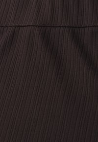 Gros plan sur un tissu côtelé brun foncé avec une couture horizontale traversant le tiers supérieur de l'image.
