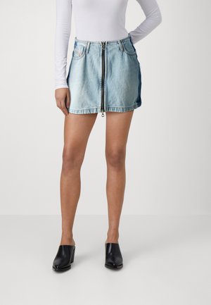 Jeans mini skjørt i lyseblå med glidelås foran, to sidelommer og rå kant. Kombinert med svarte mules.