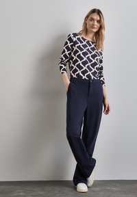 Granatowe spodnie o luźnym kroju, zestawione z kremową koszulą z granatowym wzorem z długim rękawem, charakteryzującą się okrągłym dekoltem i miękką teksturą.