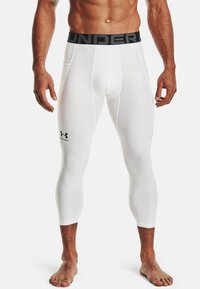 Weiße Kompressionsleggins mit einem schwarzen elastischen Bund, auf dem der Text "UNDER ARMOUR" und ein kleines Logo auf dem linken Oberschenkel zu sehen sind.