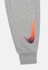 Gray sweatpants feature a ribbed cuff and a gradient orange and blue Nike logo on the side. Soft texture with a heathered finish.