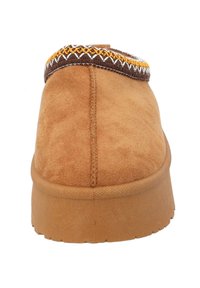 Pantofola in suede color tan con punta arrotondata, superficie testurizzata e cuciture decorative marroni e gialle attorno al collo. Suola in gomma flessibile.