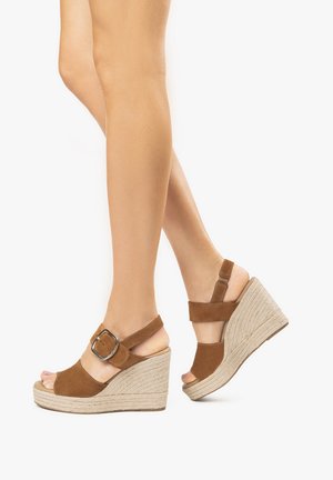 Brown suede wedge sandals with an espadrille-style sole. Features a large buckle and adjustable ankle straps. Open-toe design.