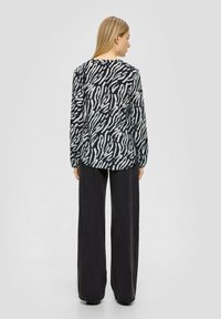 Langarmshirt mit einem schwarz-weißen Zebra-Print, abgerundetem Saum und lässiger Passform. Kombiniert mit weit geschnittenen schwarzen Hosen.
