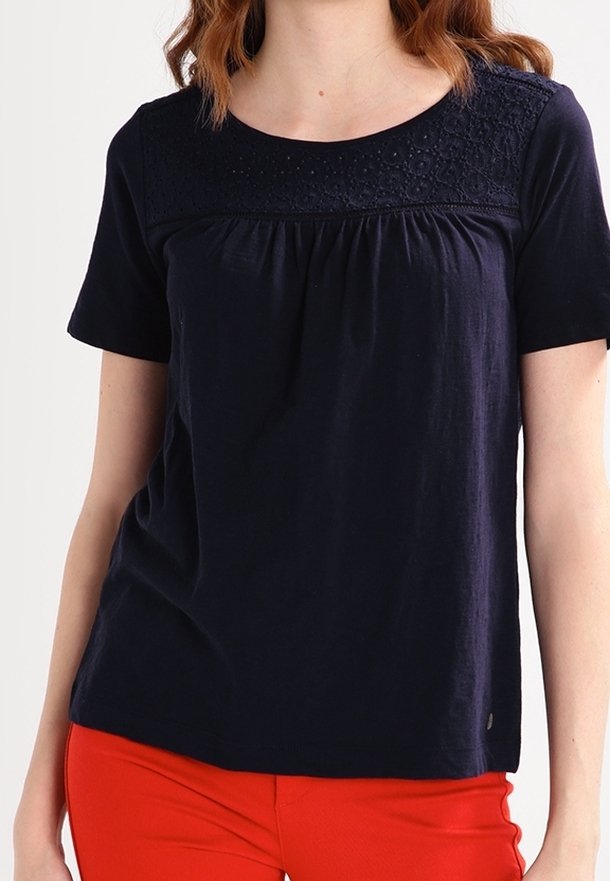 Mörkblå kortärmad topp med texturerad spetsdetalj på övre delen, draperat tyg vid midjan och en lätt A-linjeform.