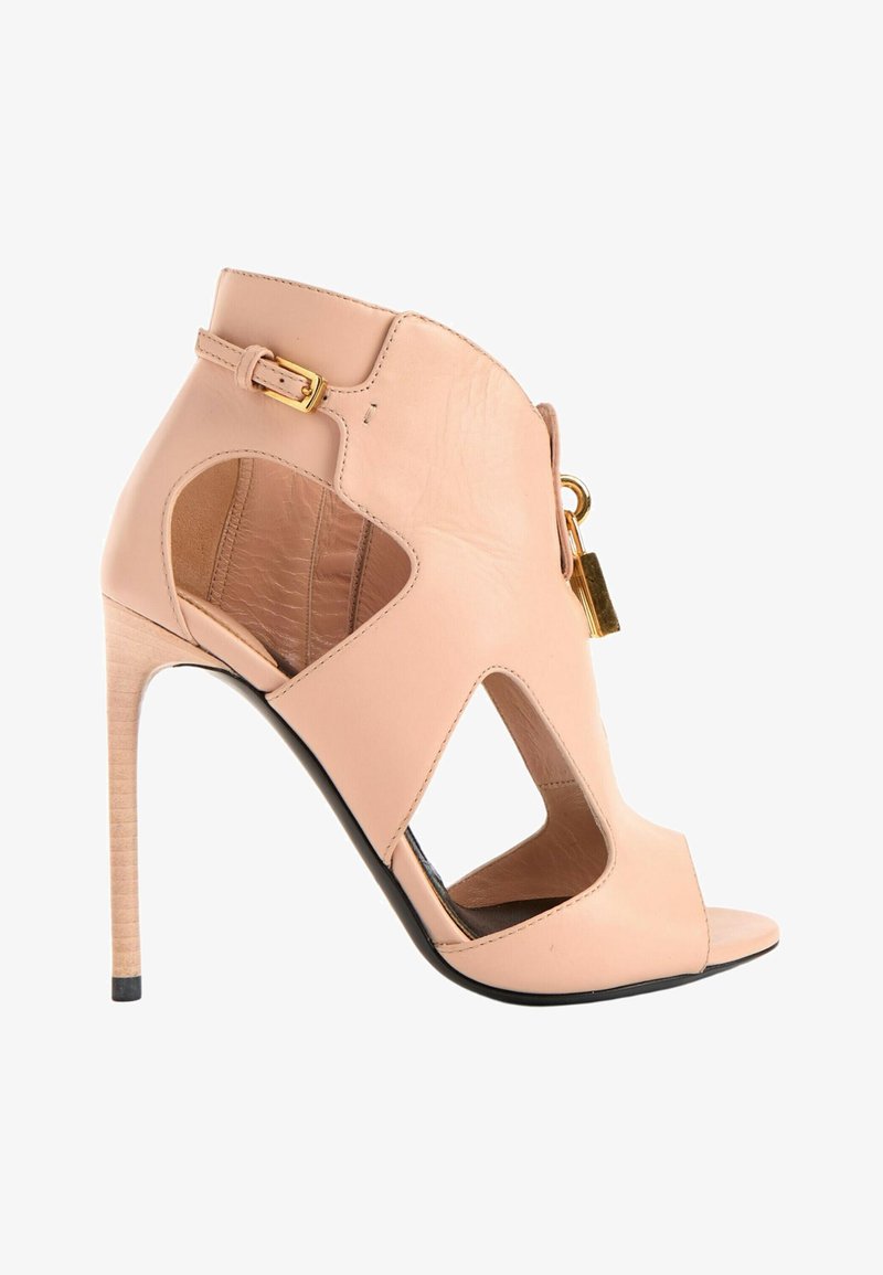 Bottine beige à talon haut et bout ouvert avec côtés découpés, bride à boucle dorée et petit détail de cadenas doré à l’avant.
