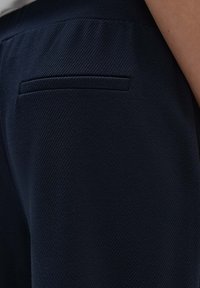 Donkerblauwe broek van een gestructureerde stof. Inclusief een slanke, paspelzak aan de achterkant, met een strakke, minimalistische uitstraling.