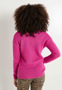 Suéter de punto rosa difuso con corte holgado, mangas largas y puños acanalados, combinado con pantalones de estampado de leopardo.