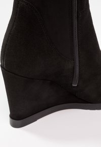 Zwarte suède sleehaklaars met een zijrits, een gladde textuur en een gevormd silhouet met een afgeronde neus en een stevige zwarte zool.