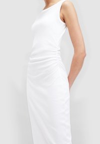 Weißes ärmelloses Kleid aus Jersey-Stoff, mit gerafften Seiten und figurbetonter Silhouette, glatter Textur und minimalistischem Design.