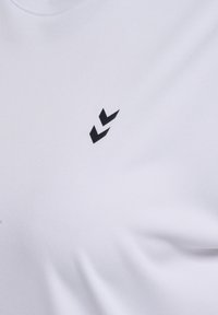 Vit t-shirt i tyg med slät textur som har en svart abstrakt logotyp på bröstet. Rund halsringning, korta ärmar.