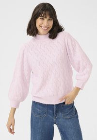 Maglione rosa lavorato a maglia con collo alto, caratterizzato da un motivo a tessitura testurizzato e maniche a sbuffo, abbinato a jeans blu.