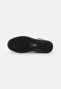 Suola di scarpa nera, caratterizzata da un motivo a zigzag testurizzato per una migliore aderenza. Un piccolo logo rosso e bianco è integrato vicino al tallone.