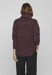 Pull en maille bordeaux avec col haut côtelé, manches longues et coupe décontractée. Surface texturée. Ourlet arrière légèrement plus long.