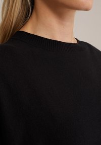 Maglione nero con scollo a girocollo a coste, realizzato in un tessuto a maglia testurizzato, che mostra un primo piano della spalla e dell'area del collo.