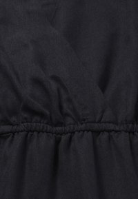 Donkere stof met een subtiele glans, met een geplooide textuur langs de naad. Gladde oppervlakte met fijne diagonale lijnen.