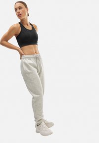 Top deportivo negro, pantalones de chándal grises con cintura elástica y cordón, combinados con zapatillas deportivas blancas. Textura suave en todo.