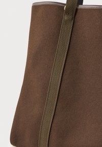 Καφέ τσάντα tote από φίλτρο με λείο υφή, διαθέτει πράσινη ραφίνα καρό και γκρίζα περιφέρεια στην κορυφή. Απλός και λειτουργικός σχεδιασμός.