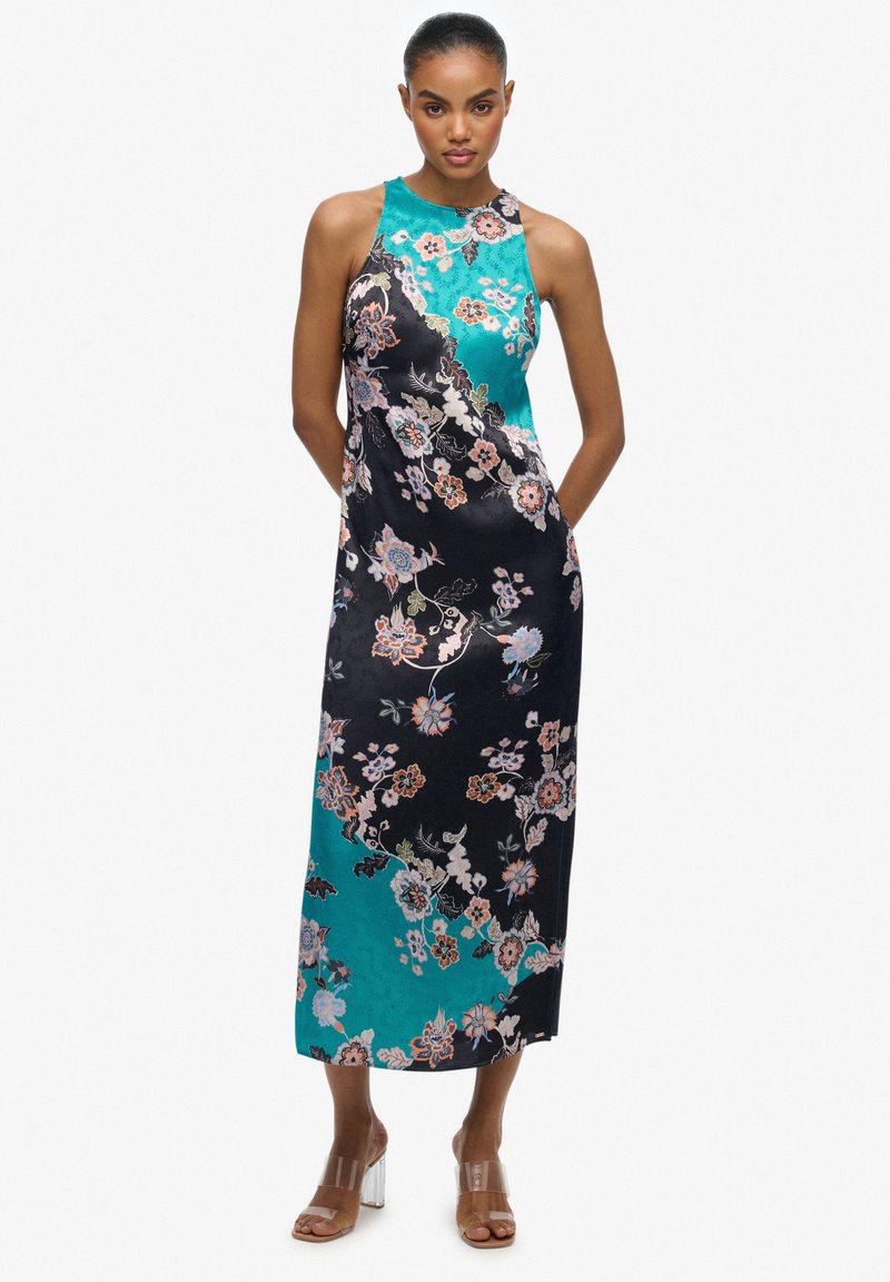 Sukienka z satyny w kwiatowy wzór w odcieniach czerni i turkusu, z wysokim kołnierzem i luźnym krojem, z widocznymi bocznymi kieszeniami i minimalnymi akcentami metalowymi.