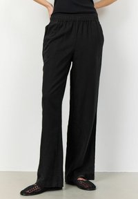Svarta, löst sittande byxor i lätt tyg med elastisk midja och sidofickor. Rätt fram med vida ben och subtil textur.