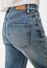 Vaqueros de denim azul claro con un acabado texturizado, que presentan una etiqueta de cuero, bolsillos traseros y costuras en contraste a lo largo de las costuras.