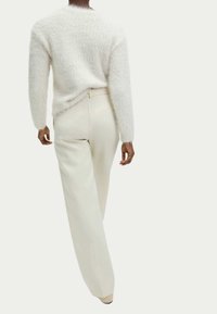 Pull fluffy blanc à manches longues associé à un pantalon large crème, doté d'une poche arrière et d'une texture lisse. Design minimaliste.