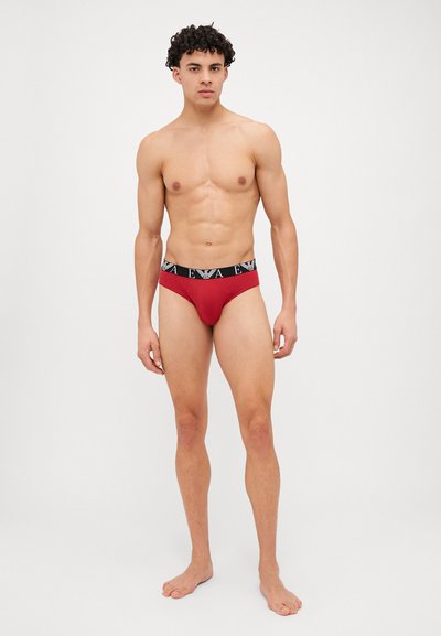 Culottes en coton rouges avec une taille noire arborant un logo blanc. Les culottes ont une coupe ajustée et une texture lisse.