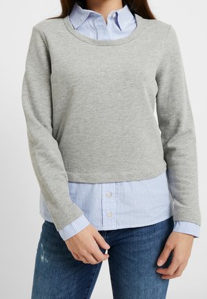 Felpa grigia a maniche lunghe sovrapposta a una camicia a righe blu e bianche con colletto. Tessuto morbido, scollatura rotonda e dettagli con bottoni sulla camicia.