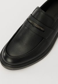 Mocassins en cuir noir avec une finition texturée. Présente un bout arrondi et lisse, ainsi qu'une bande décorative avec un accent métallique.
