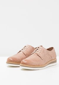 Chaussures en cuir rose clair avec un motif texturé effet peau de serpent, dotées de lacets blancs et d'une semelle beige contrastante pour plus de détails.