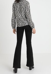 Leopardmönstrad blus i svart och beige, i kombination med svarta utsvängda byxor. Tygerna är mjuka, med en slät yta och en figursydd silhuett.