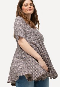 Blouse violette et crème à motifs, avec des manches courtes, un ourlet fluide et un tissu doux. Associée à un jean en denim bleu.