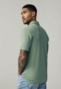 Polo de color verde claro con mangas cortas, textura suave y un cuello. Pantalones cortos de mezclilla con un corte relajado y un ligero desgastado.