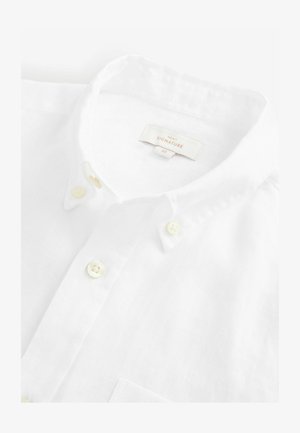 White linen collared shirt with button placket, featuring subtle texture and cream-colored buttons. Label reads "NEXT SIGNATURE" with size M.