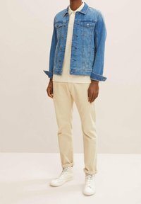 Ljusblå jeansjacka med framfickor, tillsammans med en krämfärgad polo-tröja och beiga kordbyxor. Vita högstövlar fulländar looken.