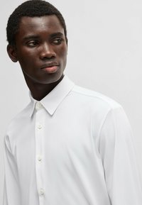 Weißes Langarmhemd mit Button-Down-Kragen, aus glattem Stoff mit feiner Textur, ausgestattet mit zwei Vorderknöpfen.