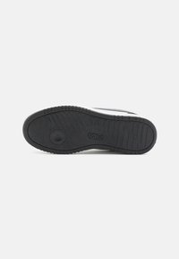 Suela de zapato de goma negra con un patrón de textura en el dibujo. Presenta un detalle del logo circular y un acento blanco a lo largo del borde.