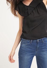 Top negro sin mangas con un escote con volantes, combinado con jeans de denim azul que presentan un diseño clásico de cinco bolsillos y un ligero desvanecimiento.